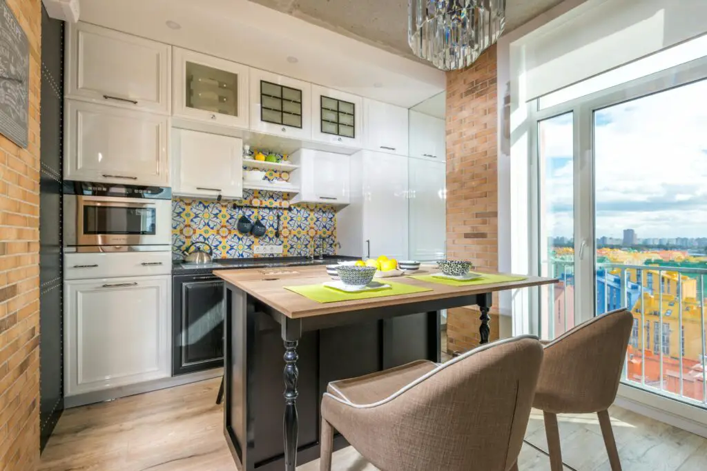 Contemporary kitchen with brick wall, colorful backsplash, and balcony view.
